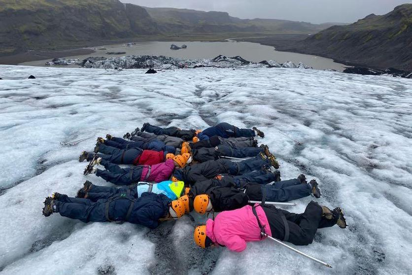 A group of students in winter gear and safety hats laying down on a lake of ice outdoors