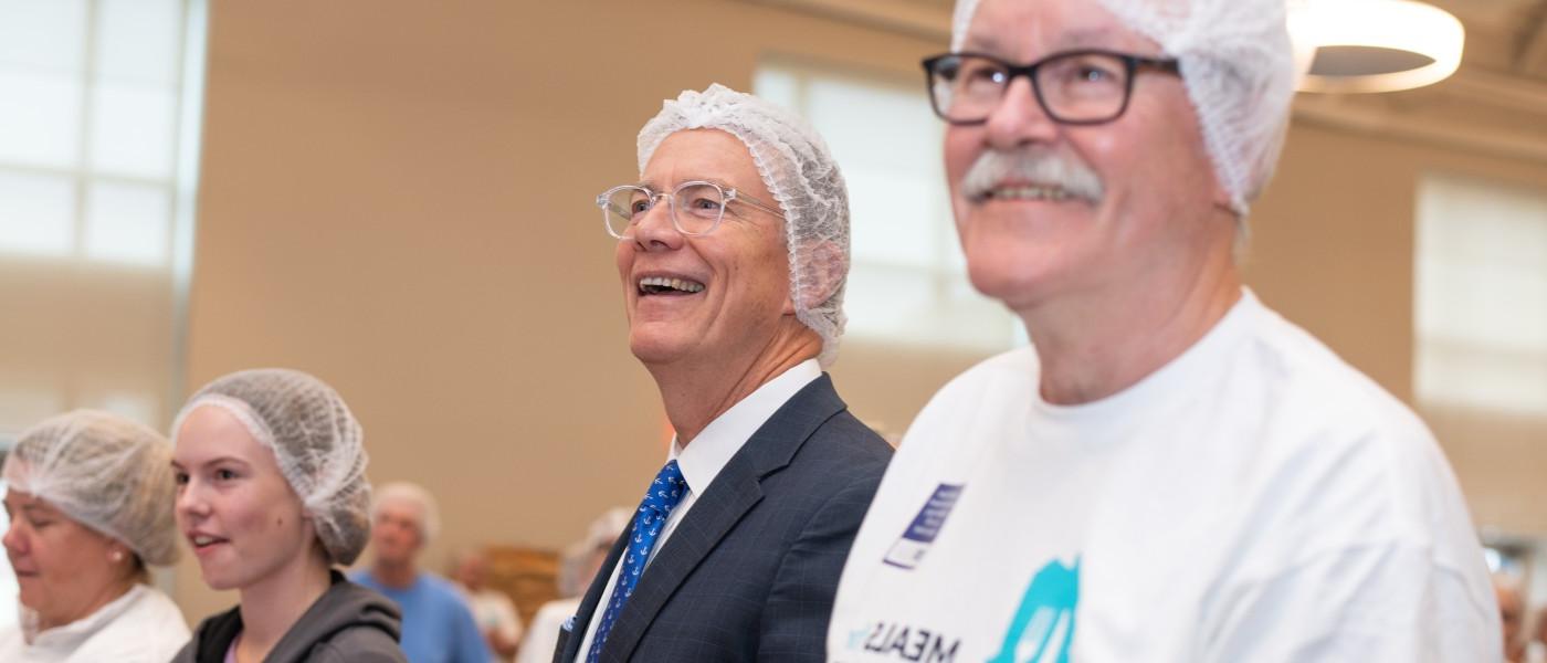 U N E President Herbert and fellow Meals for Maine volunteers wear head nets and latex gloves