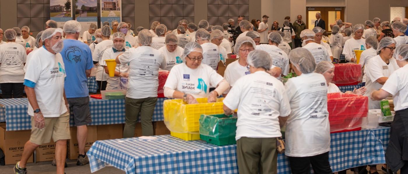 A room filled with Meals for Maine volunteers working to pack meals